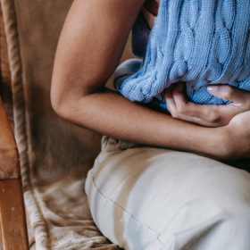 Woman in a blue jumper and cream trousers holding her tummy