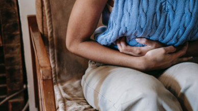 Woman in a blue jumper and cream trousers holding her tummy